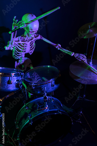 High view bony man lit by purple light with green highlights drumming