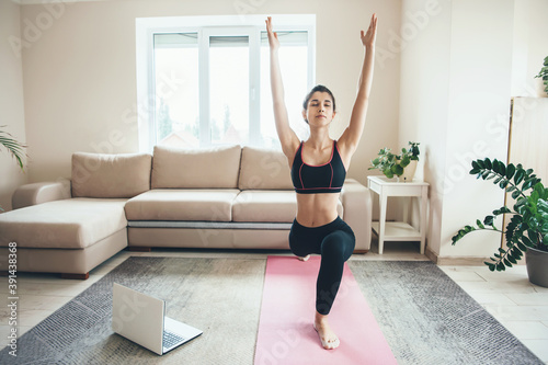 Fototapeta Naklejka Na Ścianę i Meble -  Caucasian woman stretching her body in sportswear at home during online fitness classes using a laptop