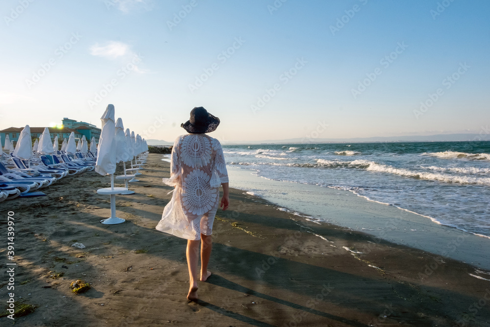 Happy girl in white bathing suit. girl walking along the beach. Girl on the shore of the ocean.
