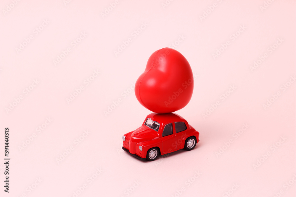 Fototapeta premium Valentines Day ,Small red retro toy car with heart on the roof on pink background. New Year, Christmas, , World Womans Day present delivery. Sale concept.object in the center