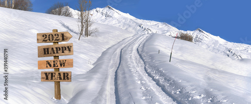 2021 happy new year written on a wooden sign in the snow in  mountain landscape