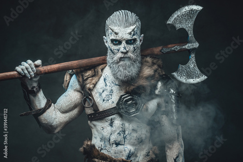 Risen from the dead northern warrior in smokey background with huge two handed axe on his shoulders staring at camera.