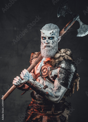 Nordic chief risen from the dead with two handed hatchet on his shoulder with horns and blue eyes in dark background.
