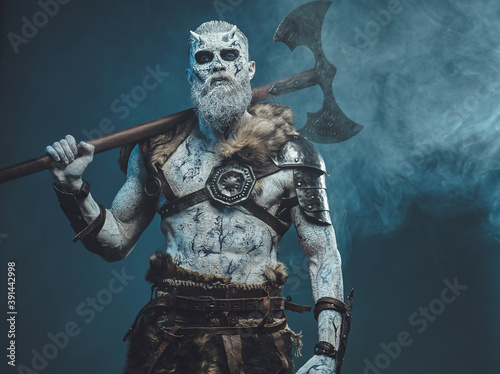 Nordic and mystical fashion undead dressed in dark armour with white hairs and skin holding two handed axe on his shoulder.