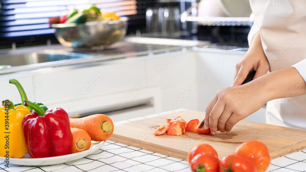 young Asian woman is preparing healthy food vegetable salad by Cutting tomato for ingredients on cutting board on light kitchen, Cooking At Home and healthy food concept. young Asian woman is preparing healthy food vegetable salad by Cutting tomato for ingredients on cutting board on light kitchen, Cooking At Home and healthy food concept.