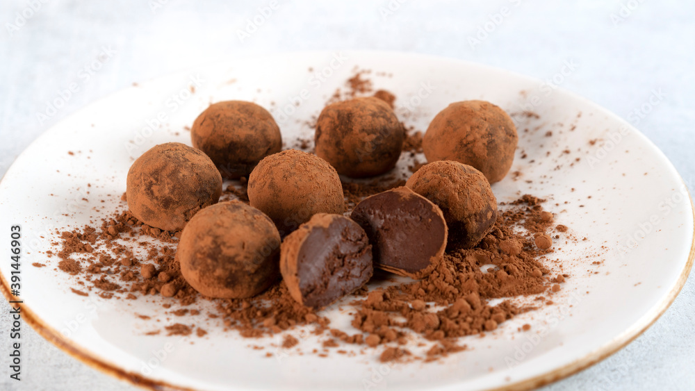 Homemade healthy tasty chocolate truffles lie on a plate. One truffle is cut in half. Delicate cream inside. Selective focus. Side view. Horizontal orientation. Homemade healthy tasty chocolate truffles lie on a plate. One truffle is cut in half. Delicate cream inside. Selective focus. Side view. Horizontal orientation.