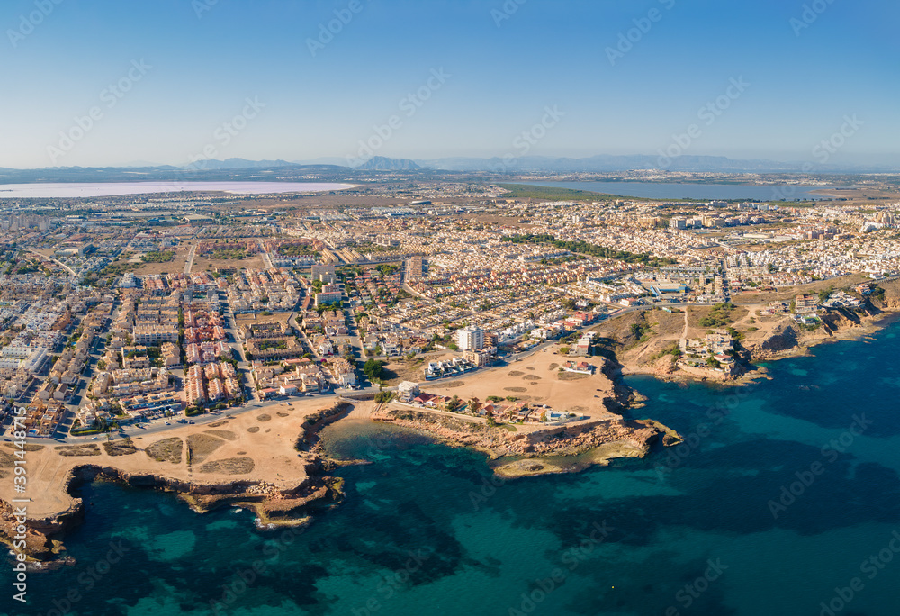 In the photo both lagoons of Torrevieja are visible. In the foreground the city with its rocky bays and the blue Mediterranean Sea. The bottom of the sea can be seen.