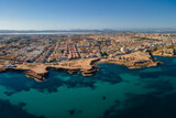 Aerial view of the city of Torrevieja on a sunny autumn afternoon with sunshine. In the foreground are rocky bays and in the background the salt lagoon.