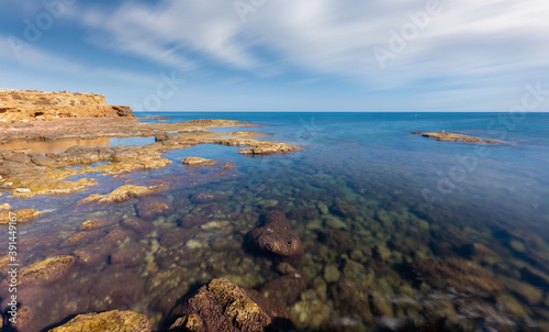 The rocky coast near the eastern Spanish city of Torrevieja in autumn. There is hardly any wind. The water is clear and you can see the sea floor and the stones. A long exposure.