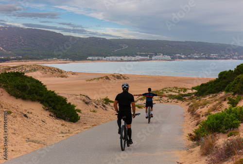 Cyclists on the otherwise deserted Atlantic beach at a camping resort north of Cape Trafalgar during the corona crisis in summer. There are some buildings in the background.