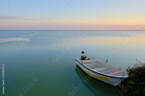Boat with an electric motor is moored to the shore. Seaside sunset with boat