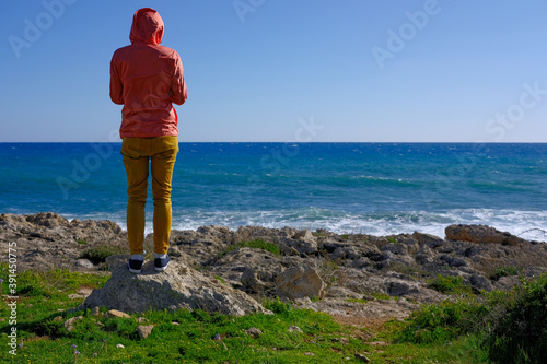 girl standing with her back to the ocean on a rocky shore on a sunny day
