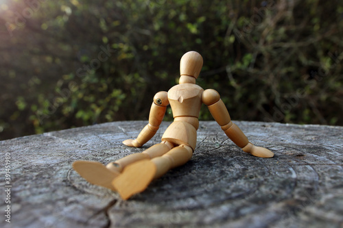 Close up of a wooden mannequin sitting outside on a tree trunk relaxing in quiet lonely forest