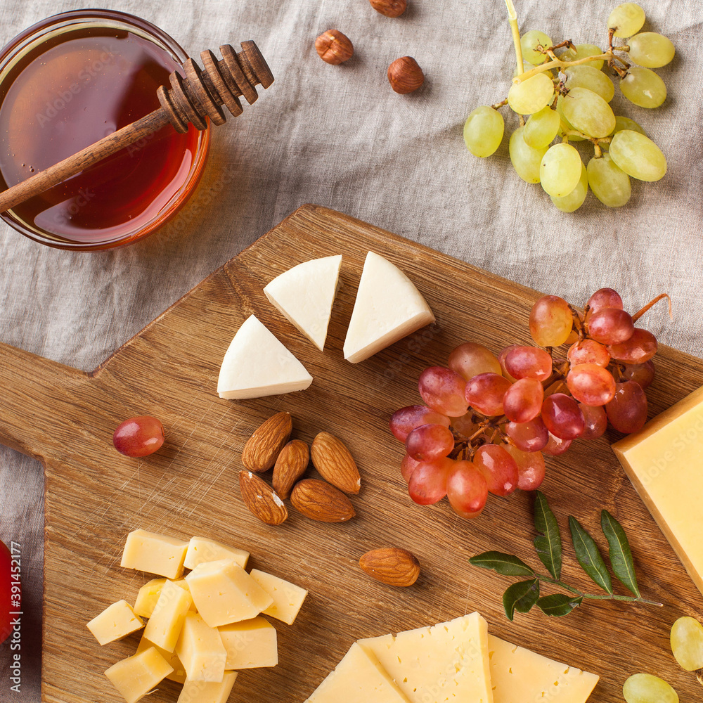 Cheese plate. Assorted cheeses on a wooden Board with grapes, honey, nuts on a linen tablecloth.