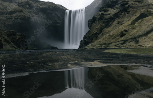 Moody dramatic long-exposure of mystical Skogafoss waterfall and reflection in southern Iceland in early spring 