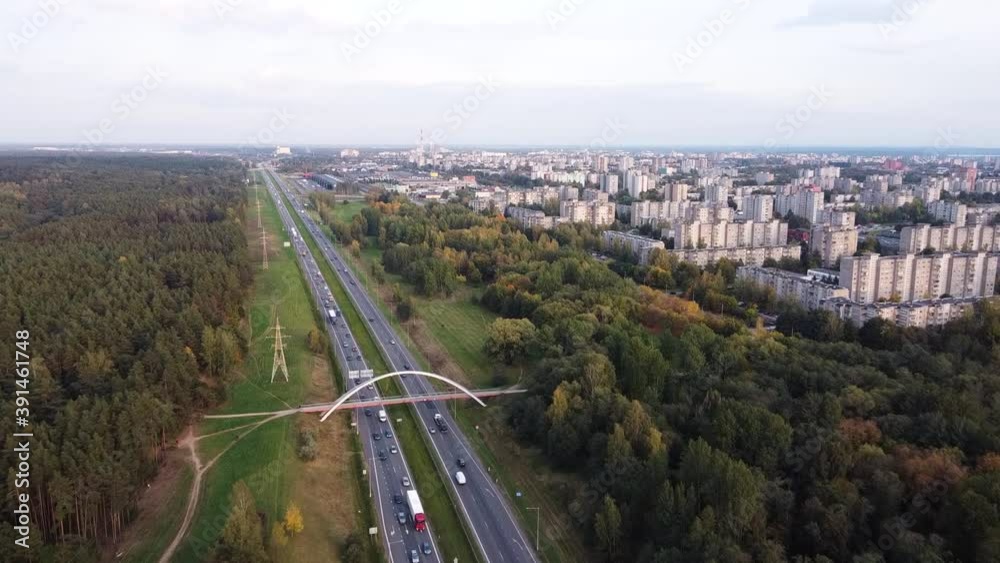 Drone slowly flying towards Kaunas city residential district over the A1 highway with heavy traffic and pedestrian bridge in the distance Drone slowly flying towards Kaunas city residential district over the A1 highway with heavy traffic and pedestrian bridge in the distance