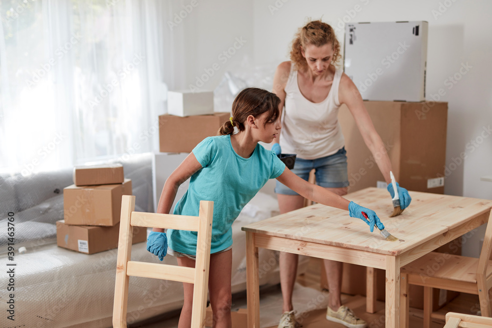 Mother and daughter painting and assembling furniture in new apartment, moving in and being hardworking.