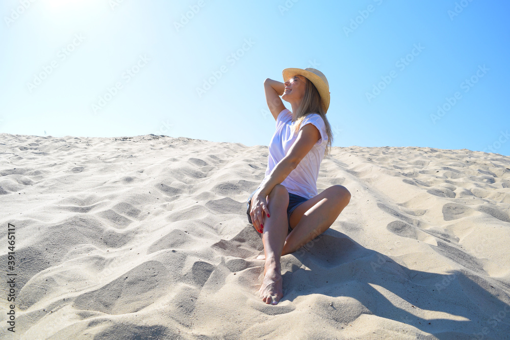 Young woman with hat sits on the sand in the desert