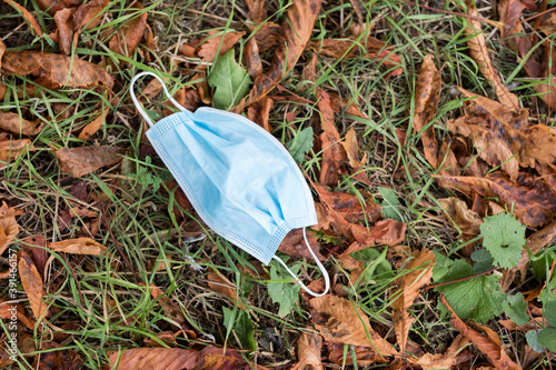 High angle close up of disposed blue surgical face mask lying on ground.