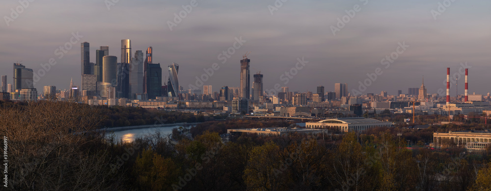 Fototapeta premium Panoramic view from Vorobyevy gory or Sparrow Hills on the Moscow city business center in the autumn evening. It is a modern complex of skyscrapers on the Moskva River embankment. Evening cityscape.