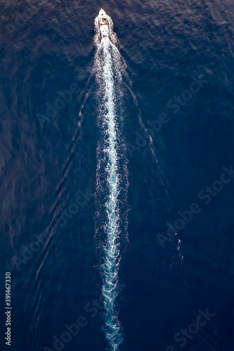 Aerial view of a boat sailing over blue water and leaving a trail of white bubbles
