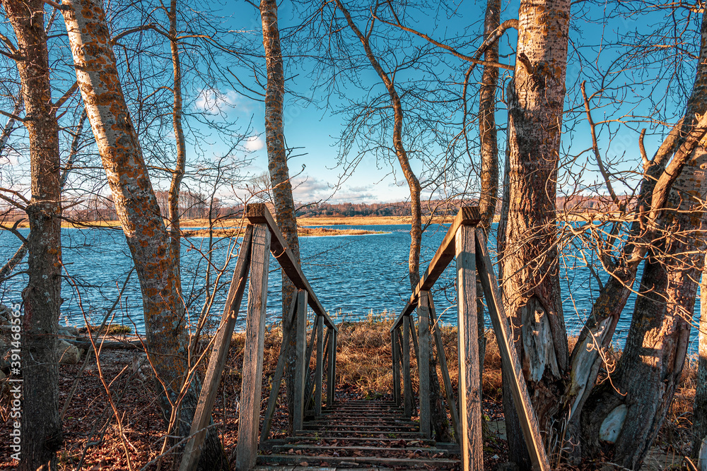 Old wooden footbridge going down to the water's edge in the river. Autumn tranquil scenery.