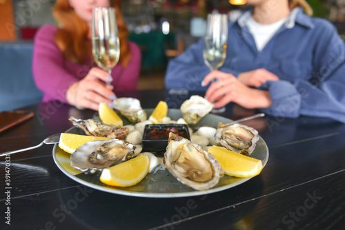 Fresh oysters as well as fine dining, two young attractive woman eating oysters in restaurant and drinking champagne.