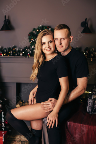 Passionate romantic couple spend time together before the New Year near a beautiful Christmas tree at home. Sexy young woman and handsome man hugging and celebrating new year