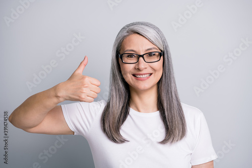 Photo portrait of smiling elder woman with grey hair showing like gesture thumb-up glasses isolated on grey color background