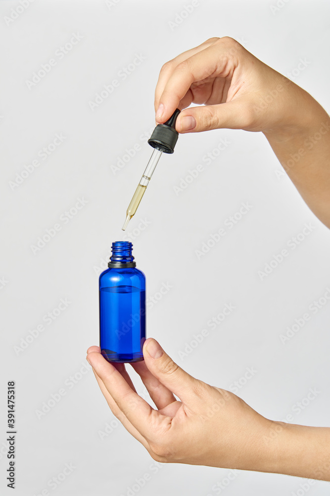 Female's hand holds a pipet of natural extract CBD oil against a light grey background.