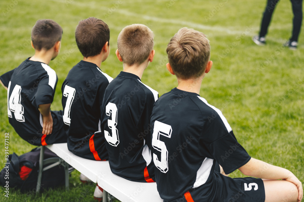 Fototapeta premium Boys in blask soccer jersey shirts sitting on football bench