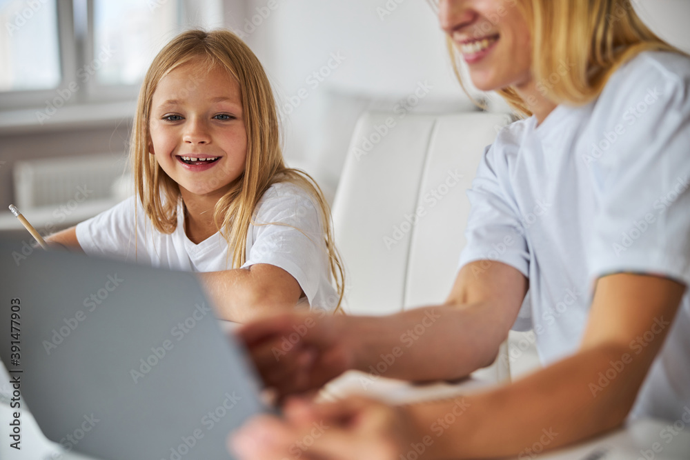 Happy smiling daughter looking to the screen laptop while sitting near mother Happy smiling daughter looking to the screen laptop while sitting near mother