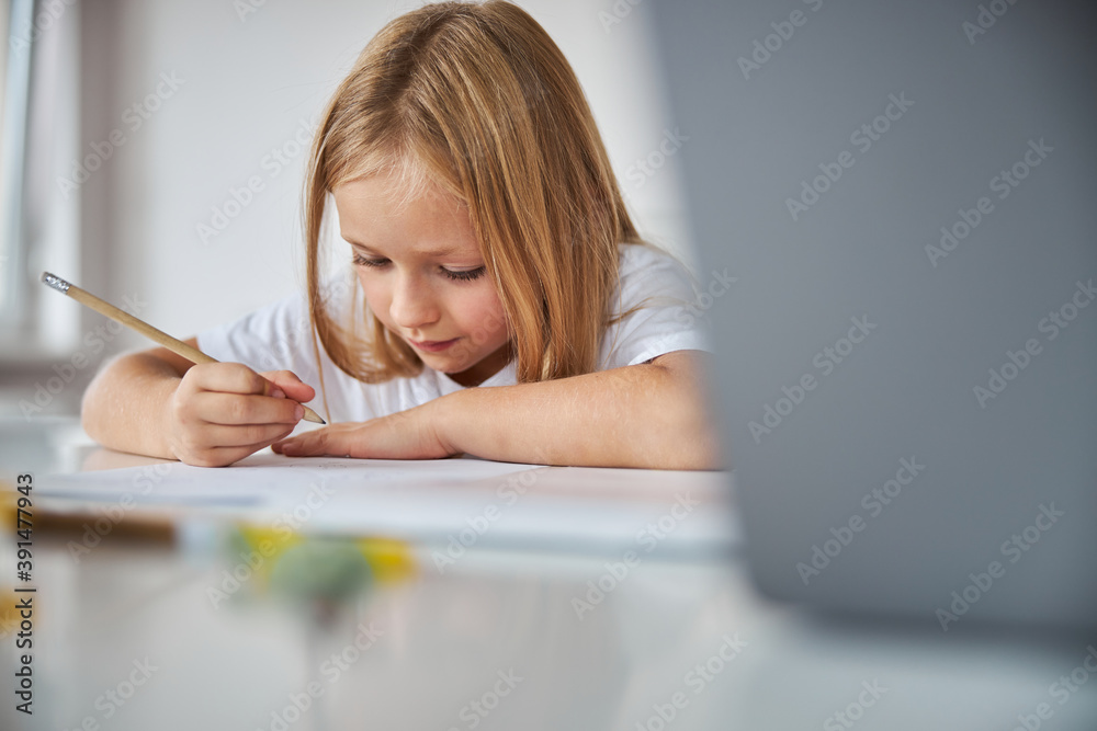 Blonde Caucasian small miss sitting at the desk while doing home work at the quarantine time in home Blonde Caucasian small miss sitting at the desk while doing home work at the quarantine time in home