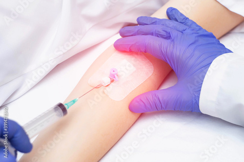 A doctor puts a venous catheter to a patient to inject drugs into a vein, close-up. Treatment