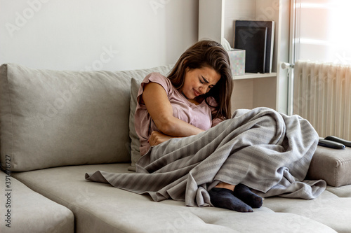 Unhappy woman holding hands on stomach suffering from abdominal pain with eyes closed. Women having menstrual period, food poisoning, gastritis or diarrhea. Girl feeling unwell sitting in living room.