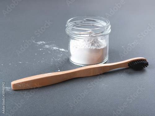 Zero waste concept for teeth cleaning. A bamboo toothbrush with toothpowder in a glass on the grey background. photo