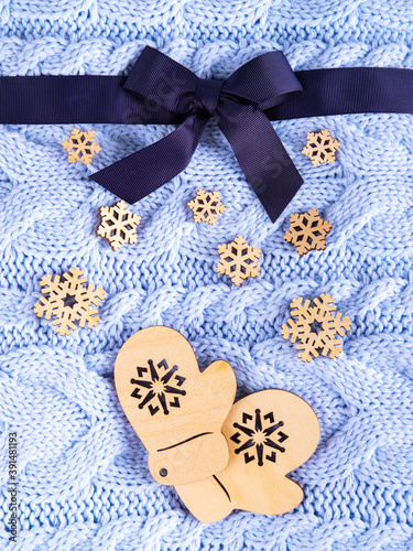 Beautiful wool knitted background in pale blue color made like a present with the ribbon and two wooden mittens and snowflakes. © Анна Авдохина