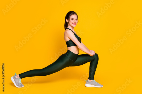 Photo of sportive young lady fitness stretching sit one leg wear sports suit top pants sneakers isolated yellow color background
