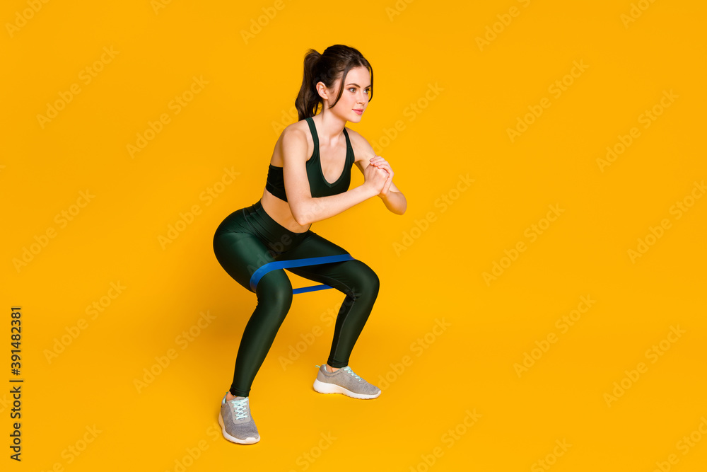 Young lady house gym training stretch resistance stripe doing squats wear sports suit isolated yellow color background