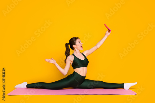 Photo of sporty lady sit mat floor stretch legs share results make selfies wear sports suit isolated yellow color background