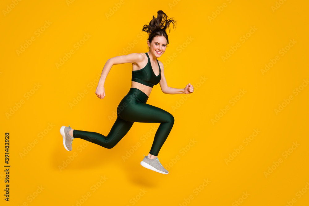 Sportive cheerful lady jump high up jogging marathon participant wear sports suit shoes isolated yellow color background