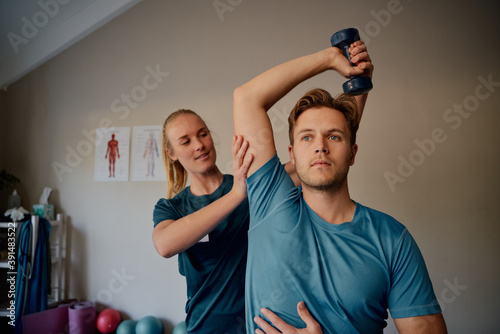 Young female physiotherapist helping patient to raise dumbbells in rehabilitation centre photo