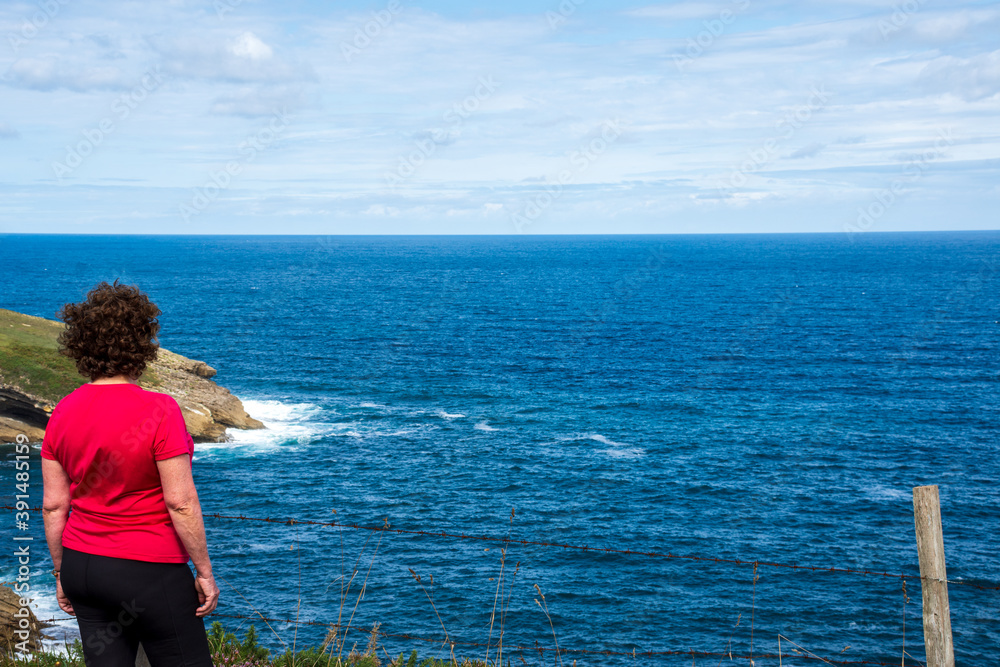 Woman from behind, wearing sportswear, looking at the landscape of the rocky coast, a sunny day, in Cantabria, Spain, horizontal Woman from behind, wearing sportswear, looking at the landscape of the rocky coast, a sunny day, in Cantabria, Spain, horizontal
