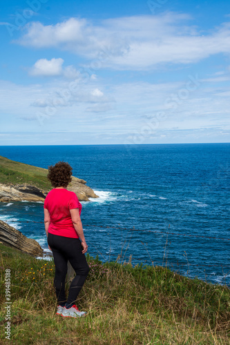 General shot of woman from behind, wearing sportswear, looking at the sea, a sunny day, in Cantabria, Spain, in portrait © Arantxa Forcada