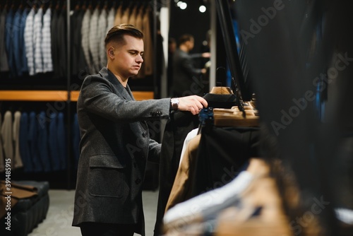 client handsome young businessman in a costume shop inspects the material of the sleeve of the jacket on the hanger.