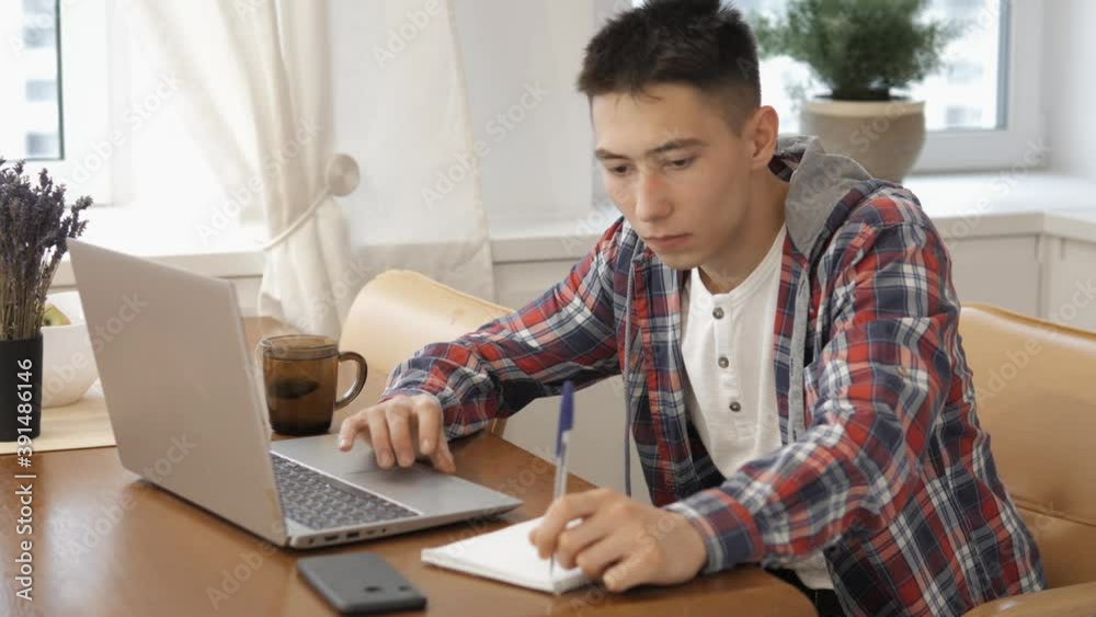 Young man using laptop texting enjoying friendly communication at home at table. Modern technology, internet and people concept, Distance education online learning lesson concept