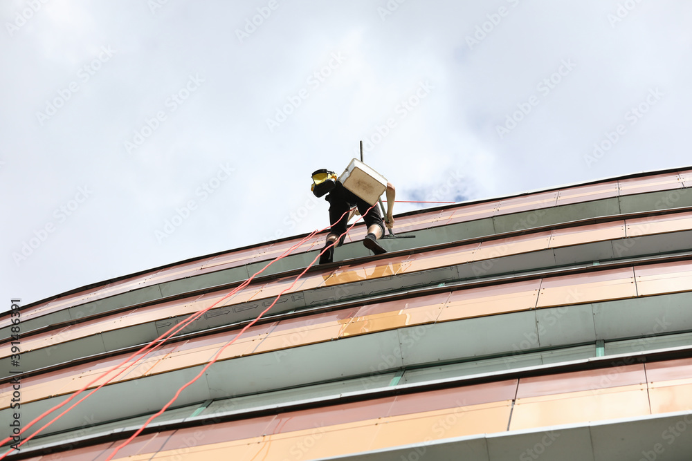 Climber hanging on ropes on building. Cleaning services for facades and windows of buildings concept