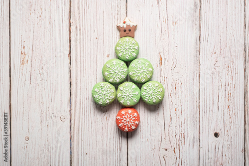 Christmas tree made from green macarons with snowflake icing decorations with gingerbread star tree topped on a white weathered wooden table background with copy space and room for text.