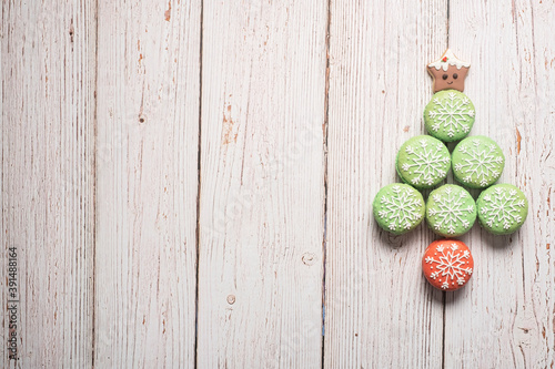 Christmas tree made from green macarons with snowflake icing decorations with gingerbread star tree topped on a white weathered wooden table background with copy space and room for text.