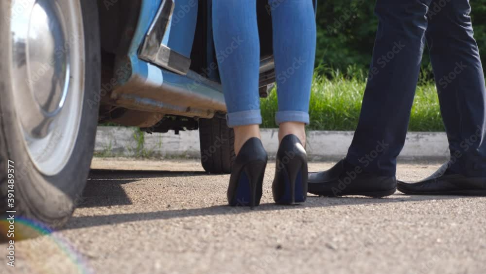 Man opens and holds door of retro car for young woman in high heels shoes. Chauffeur opening door of vintage automobile for female passenger. Legs of girl getting into old auto. Close up Slow motion